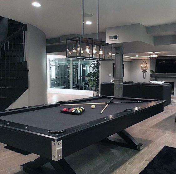 Modern masculine billiard room with black pool table, industrial pendant lighting, and spiral staircase.