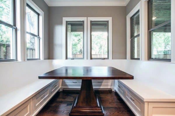 A cozy nook with a dark wooden table and white bench seating, surrounded by windows