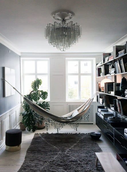Elegant hammock in a cozy living room with bookshelves, a chandelier, and large windows.