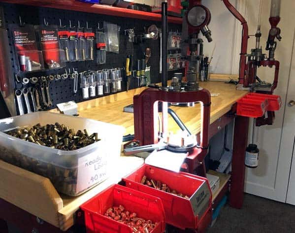 Efficient reloading bench with red presses, organized tools on a pegboard, and labeled bins for brass and bullets