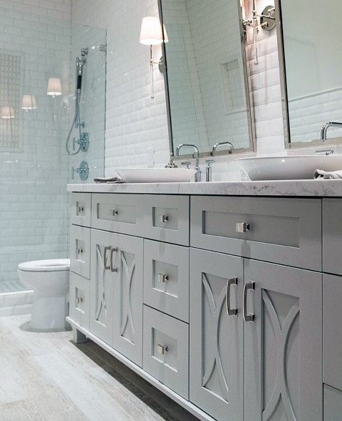 White double vanity bathroom with marble countertop, subway tile shower, and classic wall sconces.