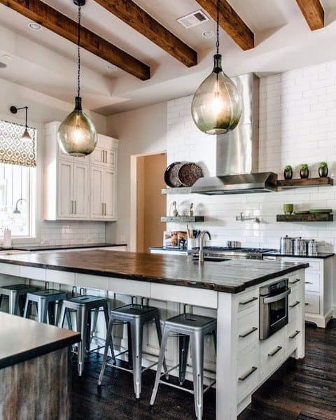 Rustic kitchen with wood-beamed ceiling, large island with dark wood countertop, and glass pendant lights.