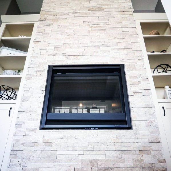 Light stacked stone fireplace with a sleek black gas insert, flanked by built-in shelves for decor