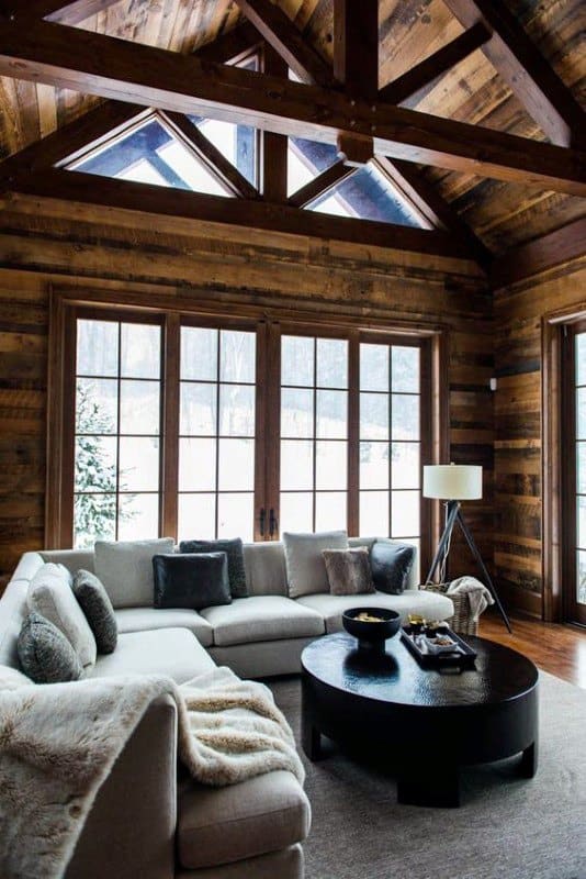 Rustic living room with wooden walls, large windows, vaulted ceiling, and cozy sectional sofa.