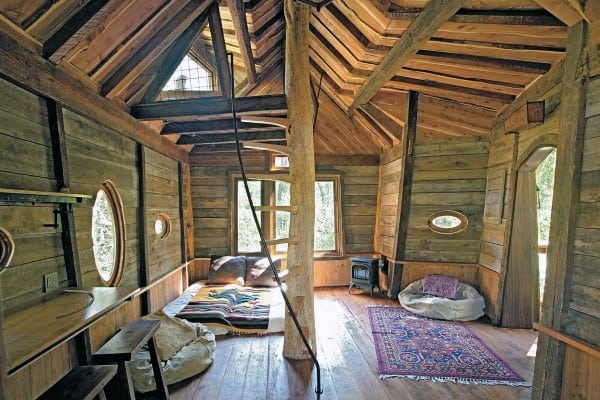 Cozy treehouse interior with wooden walls, a spiral ladder, bean bags, and a colorful rug on the wooden floor