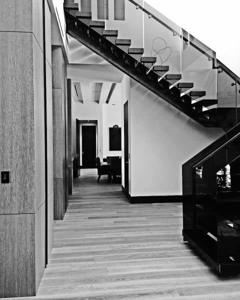 Modern black and white interior featuring a wooden staircase, glass railing, and hallway leading to distant seating