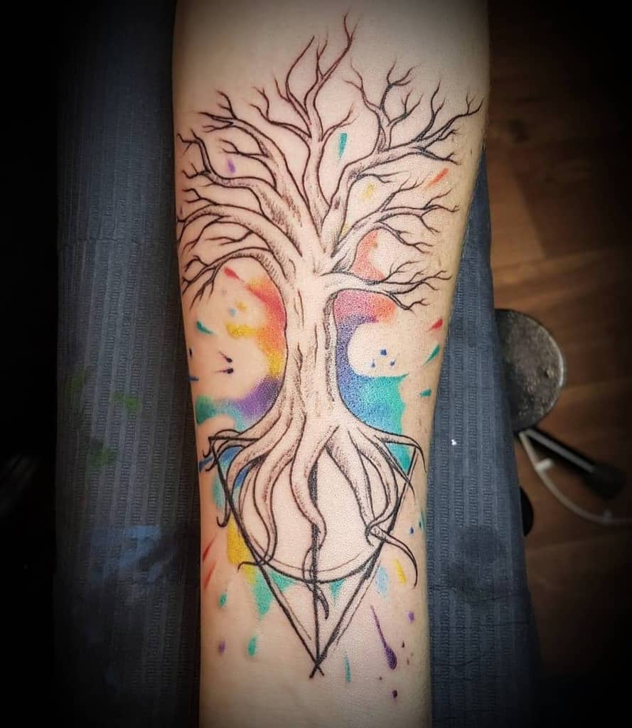 Deathly Hallows tattoo with a detailed tree growing from the symbol, featuring colorful watercolor splashes for a mystical, artistic effect.