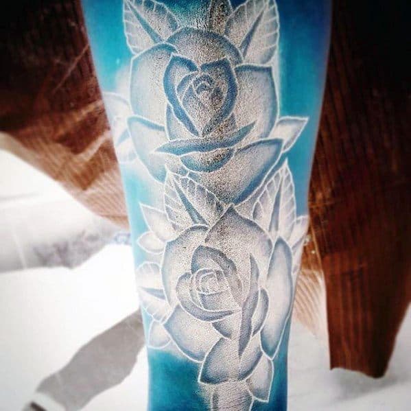 Inverted tattoo of detailed roses and leaves, glowing in white against a vibrant blue background for a striking visual effect.