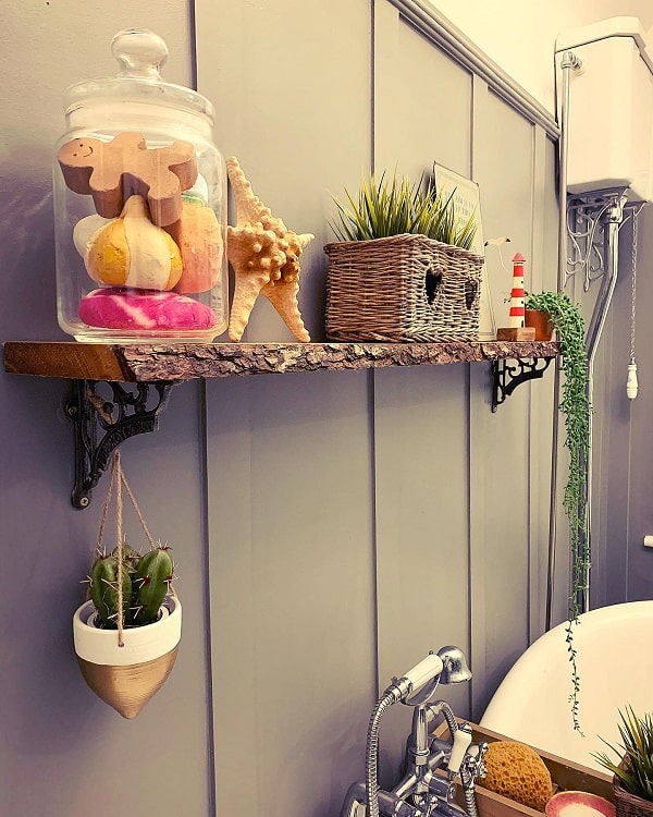 Wooden bathroom shelf with iron brackets, bath decor, plants, and glass jar with bath items.
