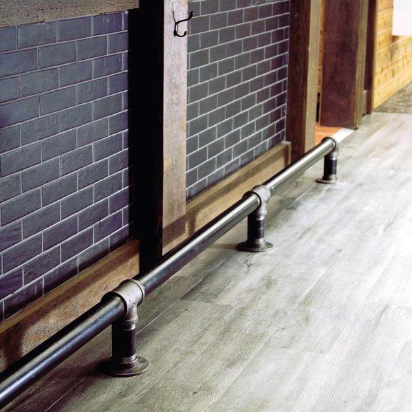 Industrial-style iron pipe foot rail attached to a wooden bar with dark subway tiles and wood flooring.