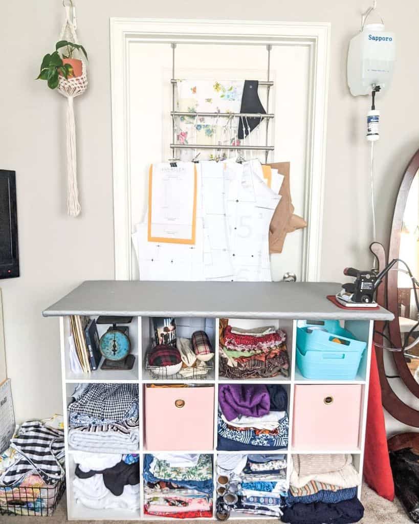 Compact sewing station with an ironing board, organized fabric storage, and pattern hanging system on the door