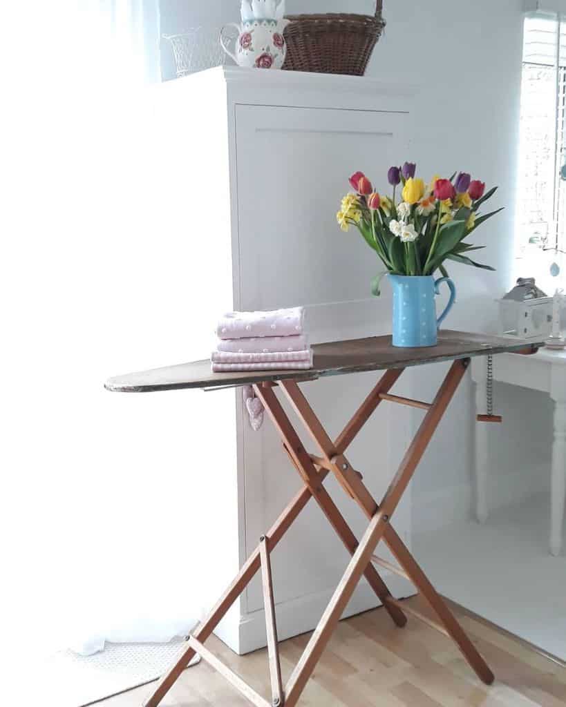 An ironing board with folded clothes and a vase of tulips in a bright sewing room