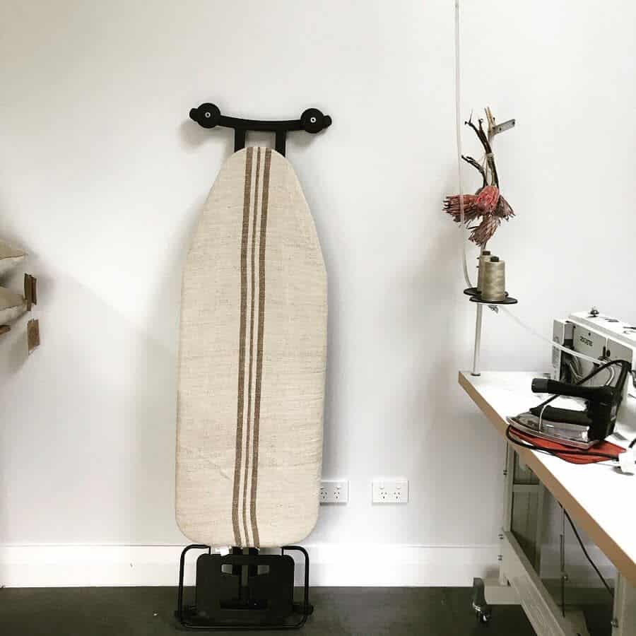 Ironing board with stripe cover in sewing room, near a sewing machine and thread spool