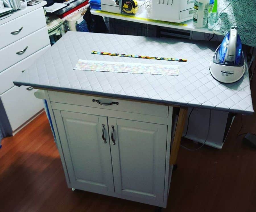 Compact sewing room with a built-in ironing board cabinet, iron, and quilting tools on a wooden floor