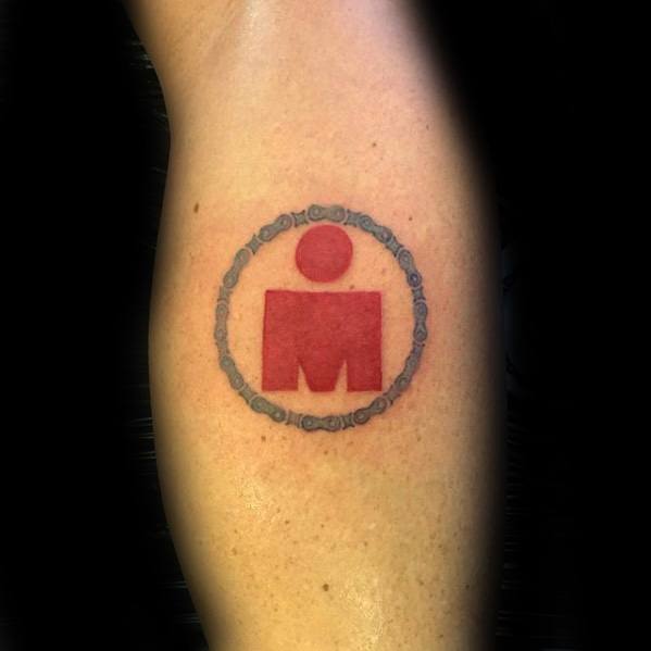Simple red Ironman logo tattoo enclosed within a detailed grey bicycle chain circle on the back of the calf.