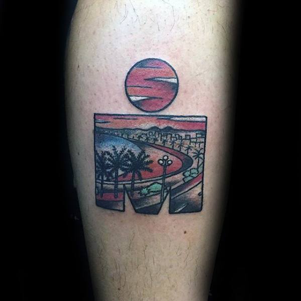 Ironman logo tattoo with a coastal cityscape, palm trees, and a red sky sunset filling the design with scenic beachside details.