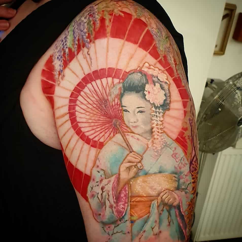 Vibrant half-sleeve tattoo of a Geisha holding a parasol, featuring soft pastel tones, floral details, and a striking red backdrop.