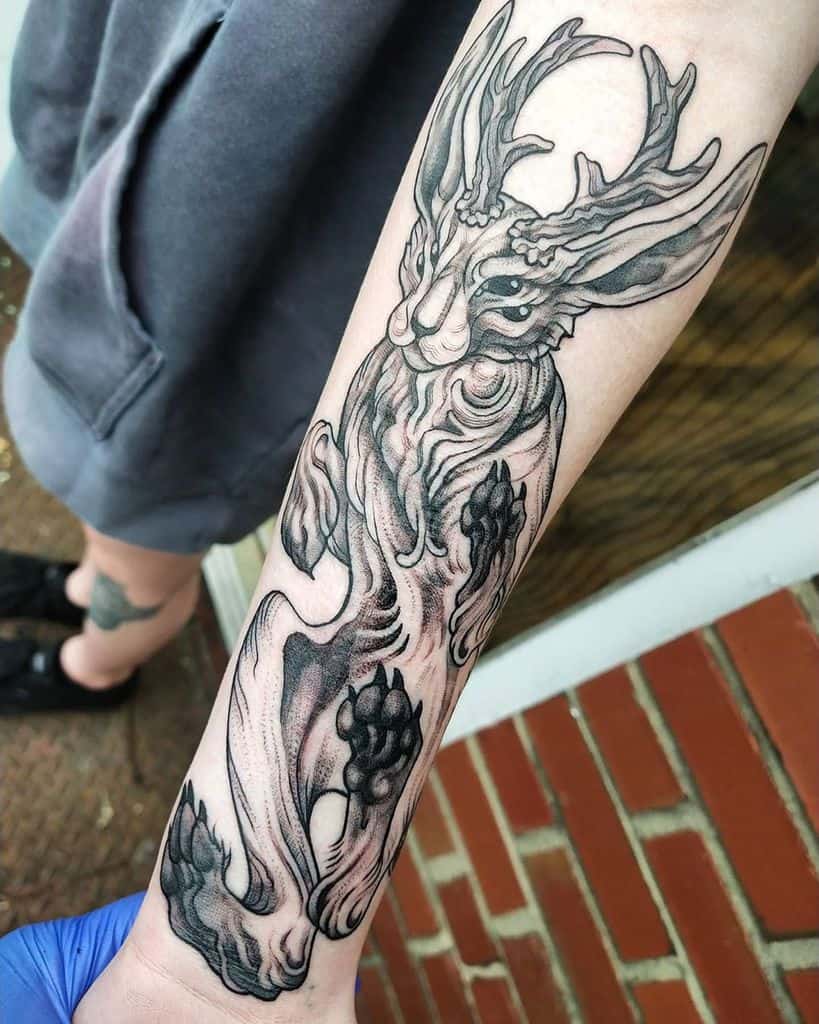 Intricate black and gray tattoo of a rabbit with antlers, including textured fur and floral accents