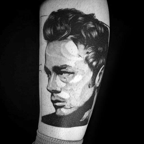 Stylized black and grey tattoo of James Dean in profile, featuring bold shadows and abstract geometric accents on the forearm.