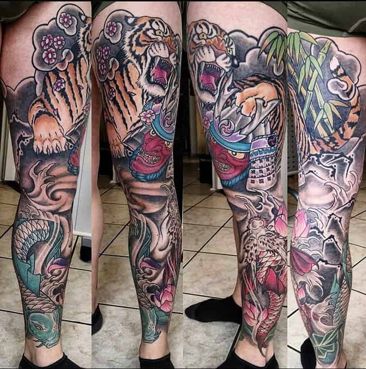 Traditional Japanese tattoo leg sleeve featuring roaring tigers, swirling clouds, a koi fish, demon samurai, dragon bamboo, and flowers