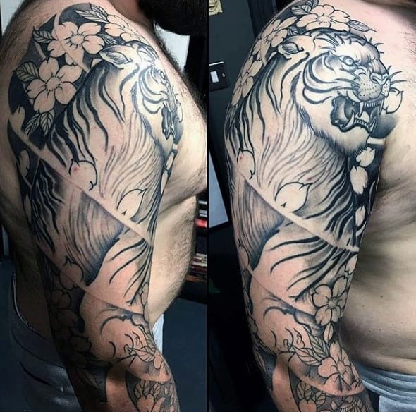 Japanese-style sleeve tattoo featuring a fierce tiger intertwined with cherry blossoms, bold shading, and a geometric sliced design effect