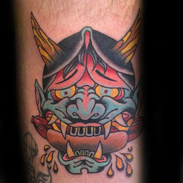 Tattoo featuring a colorful and detailed Japanese-inspired demon mask with sharp teeth and fierce expression, on the forearm.