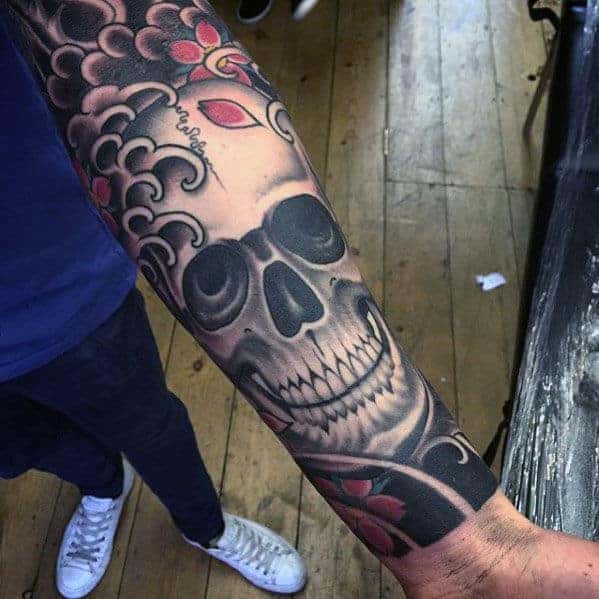 Arm tattoo featuring a large skull with floral and cloud designs