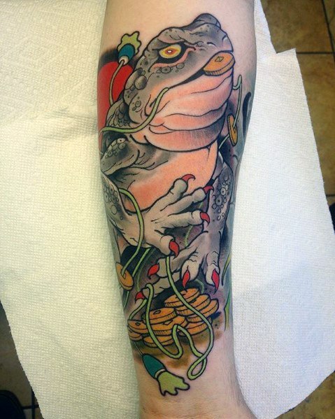 Japanese-style forearm tattoo featuring a large mystical toad clutching gold coins, with flowing ribbons and bold traditional shading for a striking look.