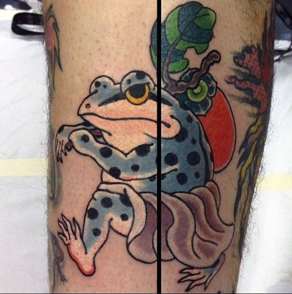 Japanese-style tattoo of a blue-spotted frog wearing a flowing robe, positioned across two legs, creating a seamless design when joined together.