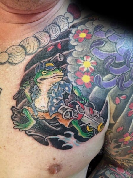 Japanese-style chest tattoo featuring a warrior frog in traditional attire, gripping a gun, surrounded by swirling waves, cherry blossoms, and bold patterns.