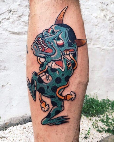 Japanese-style tattoo featuring a blue-spotted frog carrying a traditional Hannya mask, symbolizing transformation, mystery, and folklore-inspired themes.