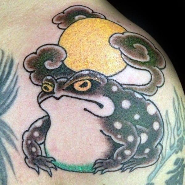 Japanese-style tattoo featuring a black and white spotted frog sitting beneath a golden sun, surrounded by stylized clouds, symbolizing wisdom and serenity.