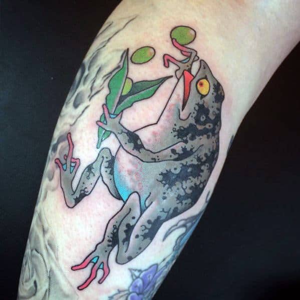 Japanese-style tattoo featuring a black-spotted frog holding a leafy branch with berries, set against a flowing background, symbolizing nature and balance.