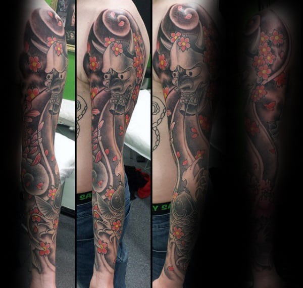 Japanese-style full sleeve tattoo featuring a fierce samurai mask, koi fish, swirling clouds, and vibrant cherry blossoms with falling petals