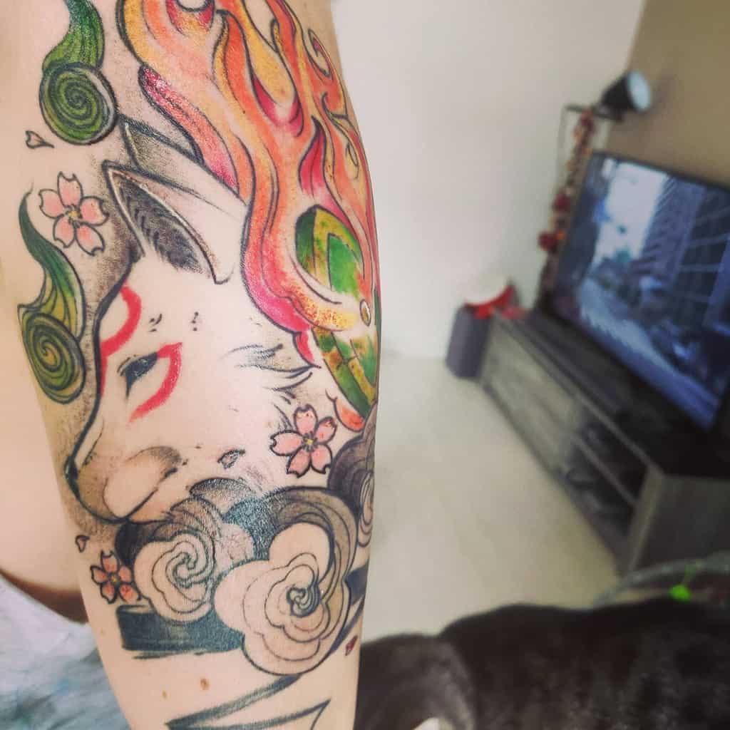 Colorful Okami tattoo featuring Amaterasu with flowing flames, cherry blossoms, and swirling clouds, blending traditional Japanese aesthetics