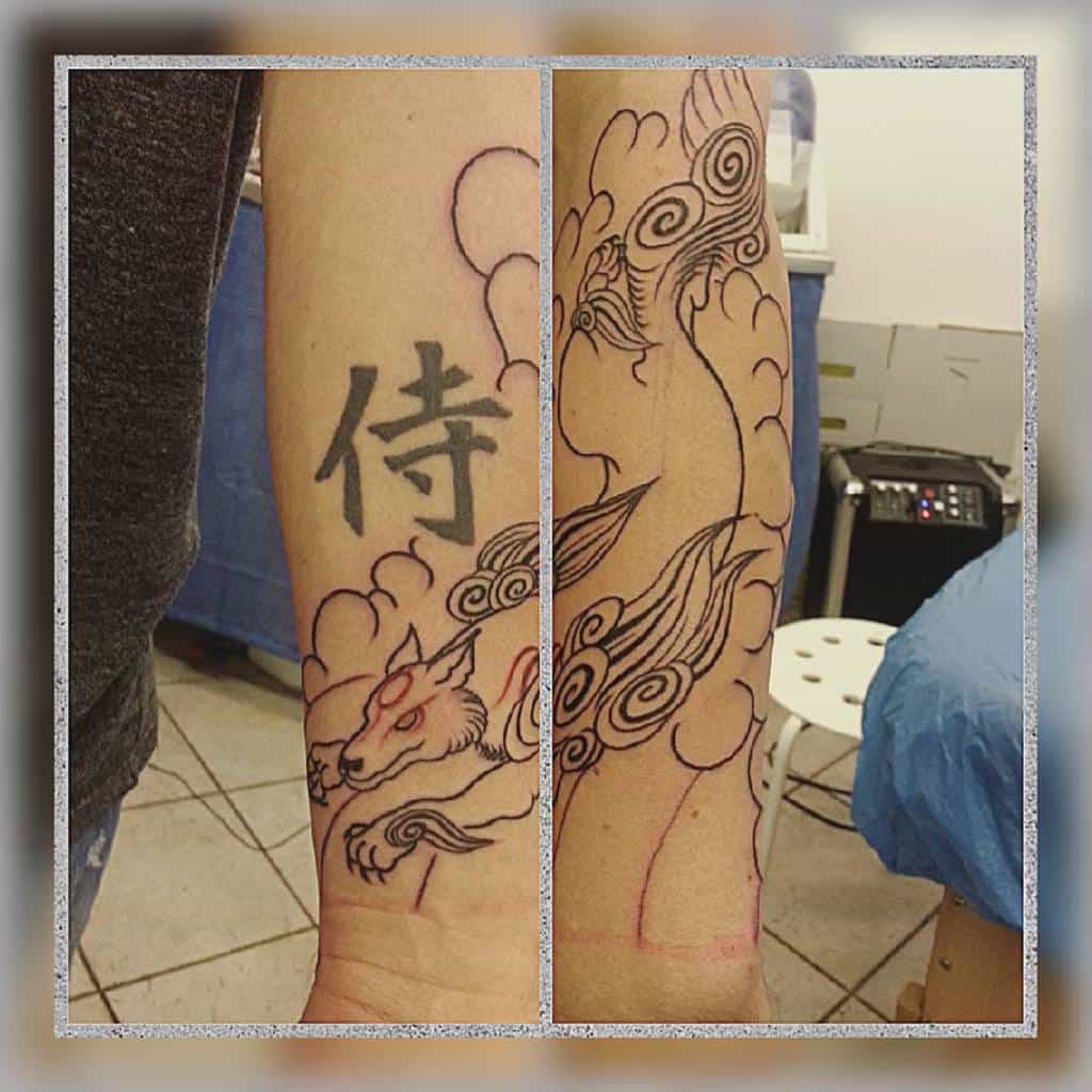 Black and red Okami tattoo in progress, featuring Amaterasu with swirling clouds and a kanji symbol, blending traditional Japanese elements