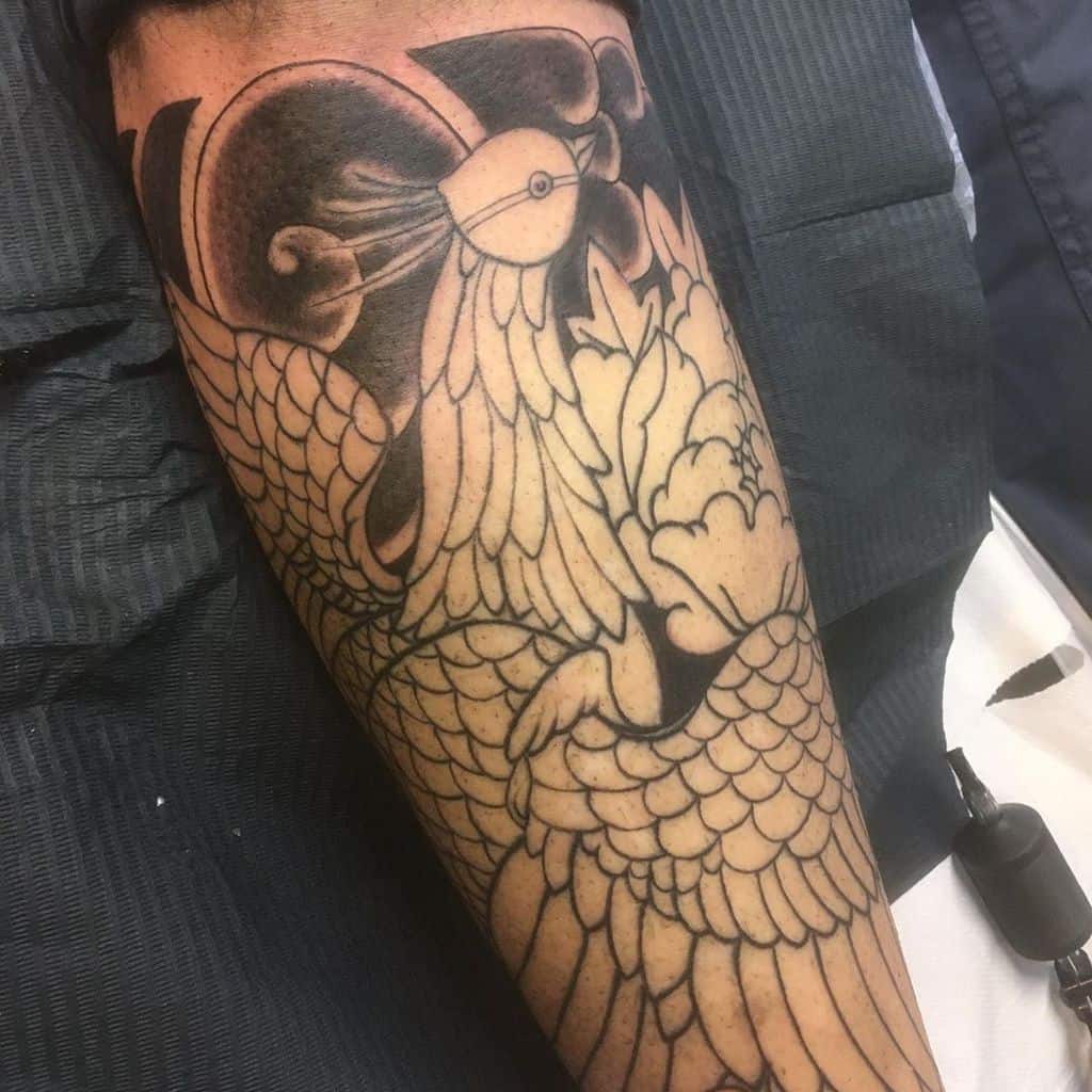 Black ink peacock tattoo in progress, featuring intricate feather details and flowing lines.