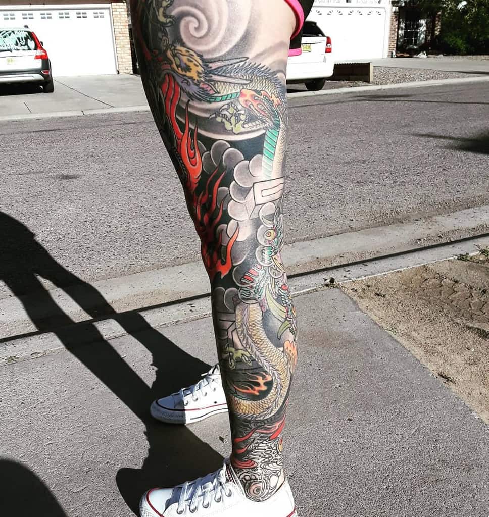Traditional Japanese tattoo leg sleeve featuring a detailed dragon, surrounded by swirling clouds, fiery accents, and bold black and red shading