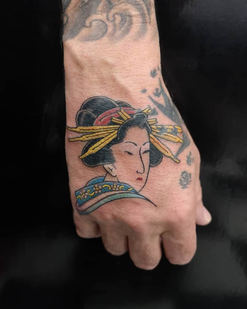 Traditional Japanese-style hand tattoo of a Geisha with an ornate hairstyle, golden hairpins, and a colorful kimono, featuring bold outlines.