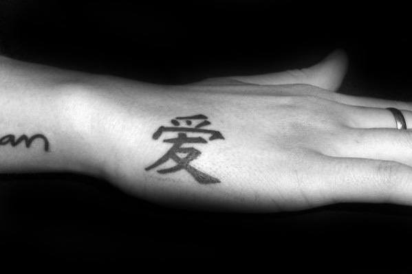 Side hand tattoo for men with a bold black Chinese character for love, placed prominently near the thumb area.