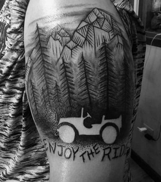 Black and grey tattoo of a Jeep silhouette with "Enjoy the Ride" text, set against a forest and mountain landscape with detailed shading.