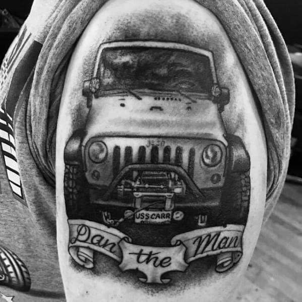 Realistic black and grey tattoo of a Jeep Wrangler front view with intricate shading, featuring a banner below that reads "Dan the Man."