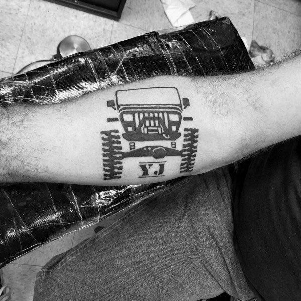 Bold black ink tattoo of a Jeep YJ front view with tire tracks, placed on the forearm, symbolizing off-road adventure and Jeep passion.