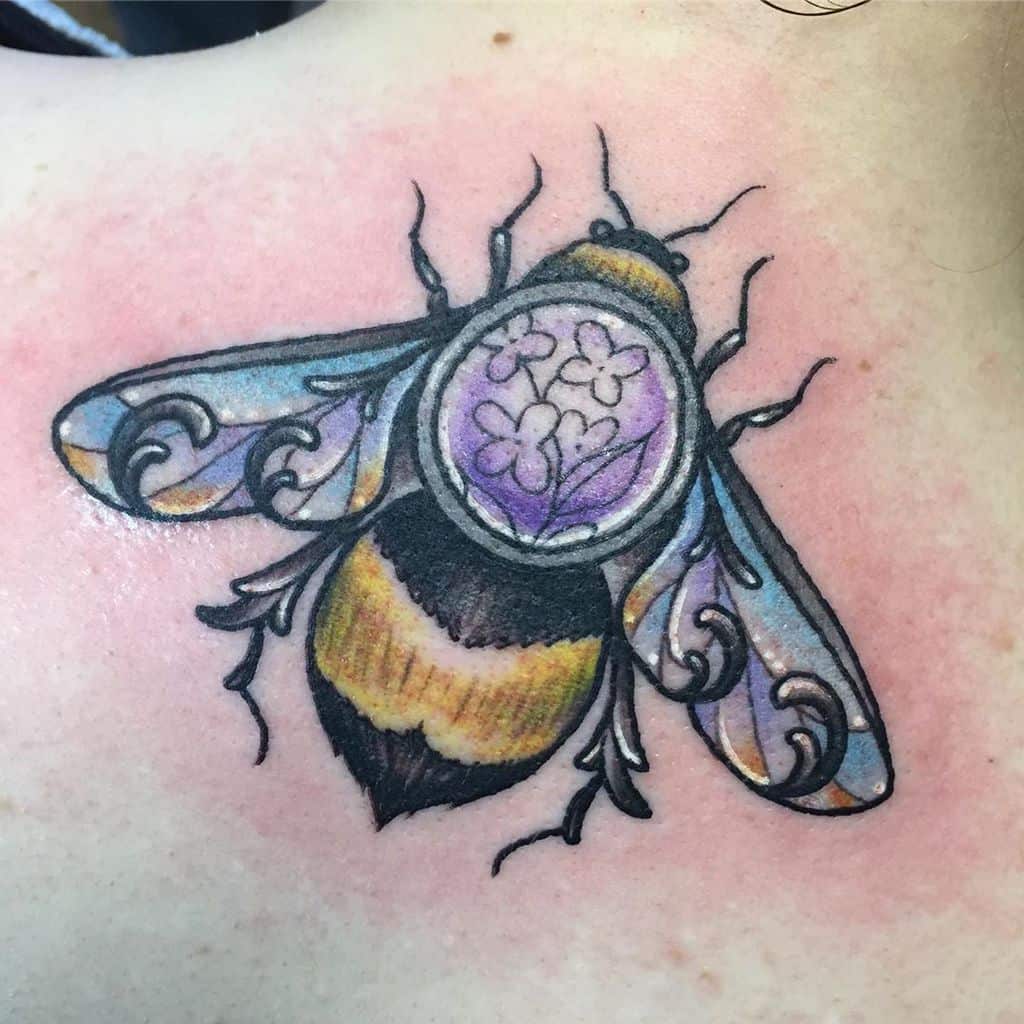 Colorful tattoo of a bee with ornate wings and a lilac flower design within its body, blending realism with decorative elements.