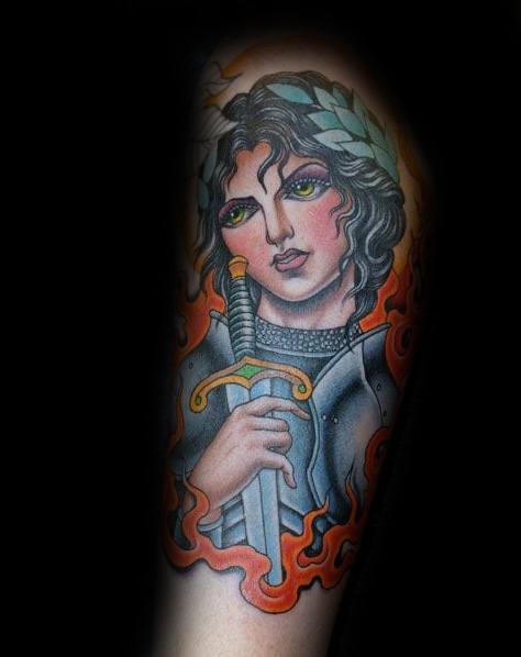 Vibrant Joan of Arc tattoo with piercing green eyes, laurel crown, and flaming sword, blending realism with bold neo-traditional flair.
