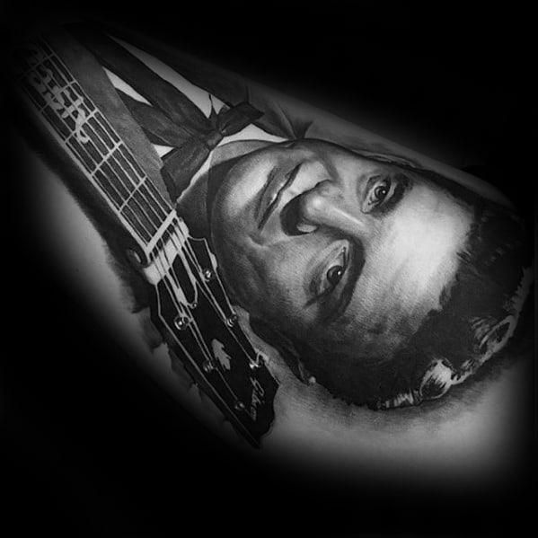 Tattoo of Johnny Cash with a guitar on a forearm, in black and white