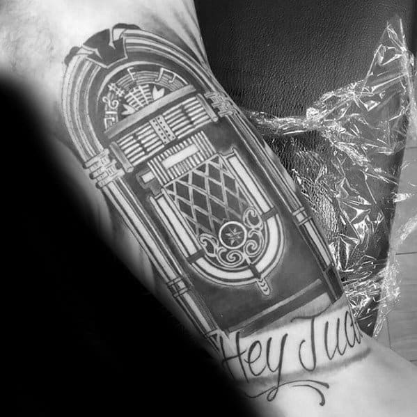Black and gray tattoo of a vintage jukebox with musical notes, paired with elegant script reading "Hey Jude" as a tribute to The Beatles.