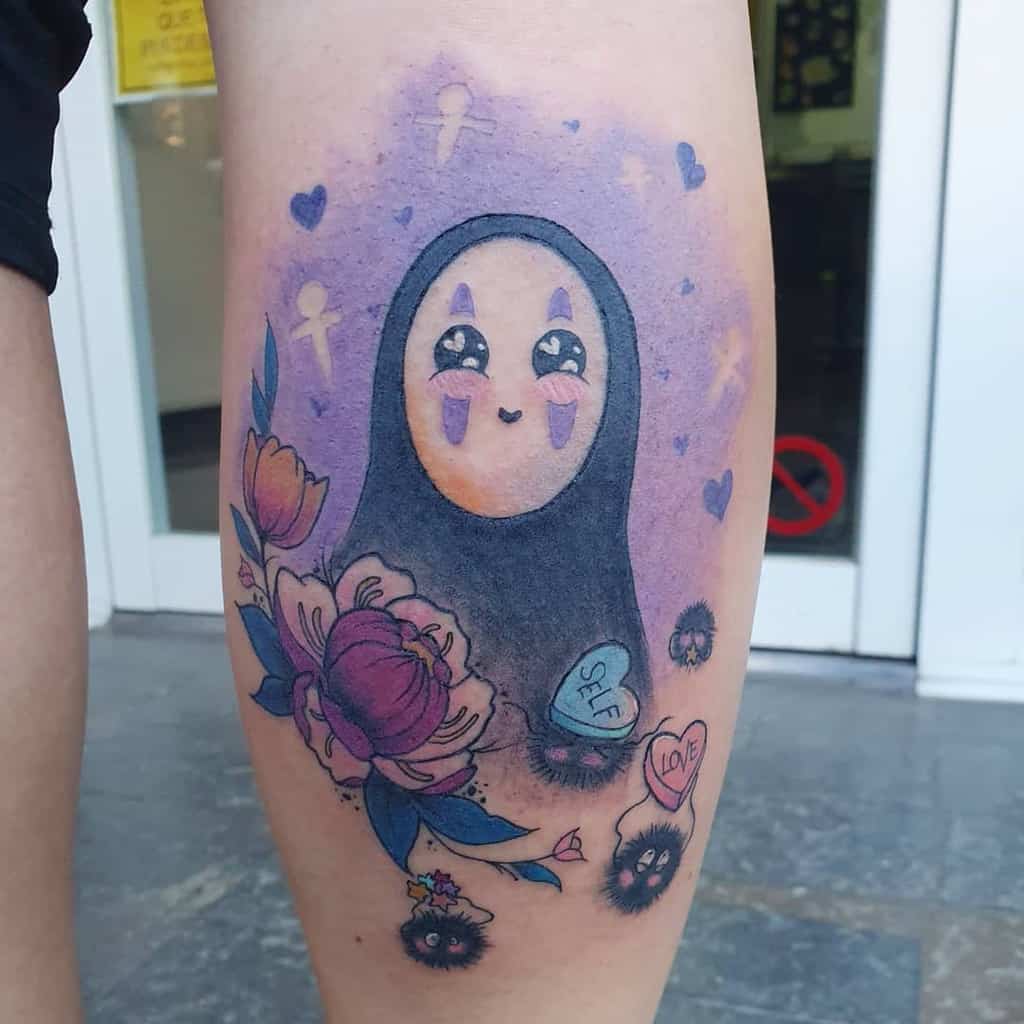 Cute pastel Spirited Away tattoo of No-Face with a happy expression, surrounded by flowers, soot sprites, and heart-shaped candies on a purple background