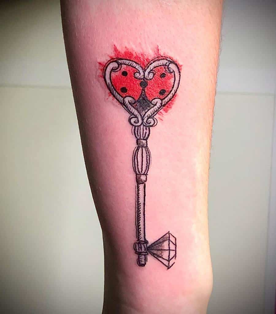 Elegant key tattoo with a heart-shaped ladybug design at the top, intricate detailing, and a diamond-shaped tip, accented with red shading.