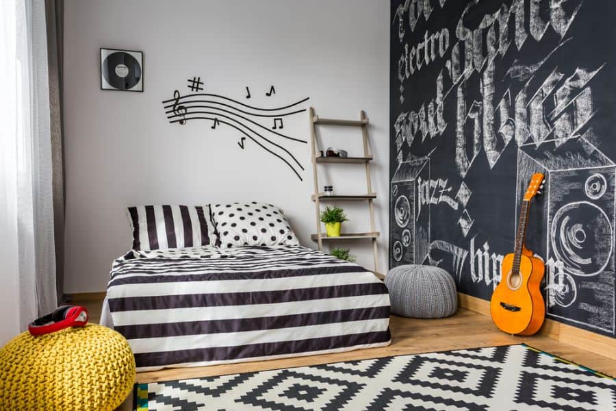 Music-themed bedroom with striped bedding, chalkboard wall, and acoustic guitar decor.